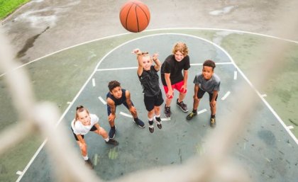 A group of teenagers standing on a basketball court in anticipation as a basketball sinks into a hoop